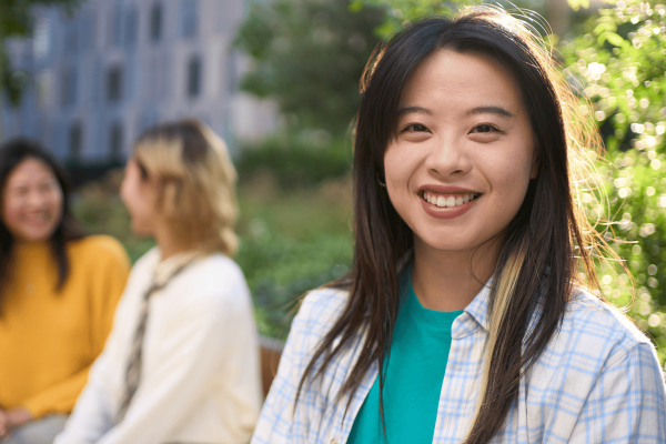 Young asian women smiling at the front of the photo with two women sitting on the bench behind her out of focus