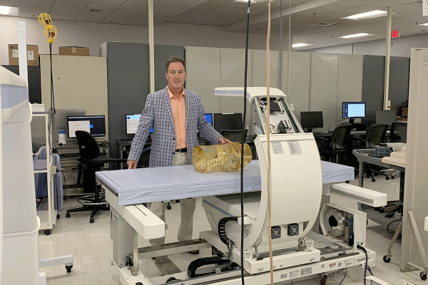 Man in blue jacket stand behind a medical device. 