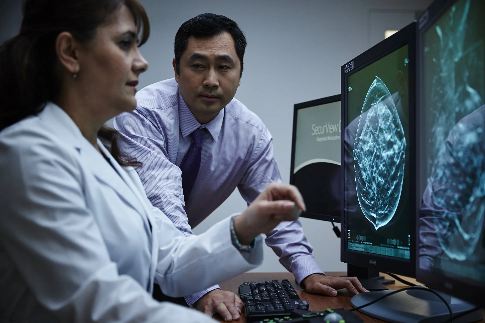 2 healthcare professionals looking at mammography images on screens