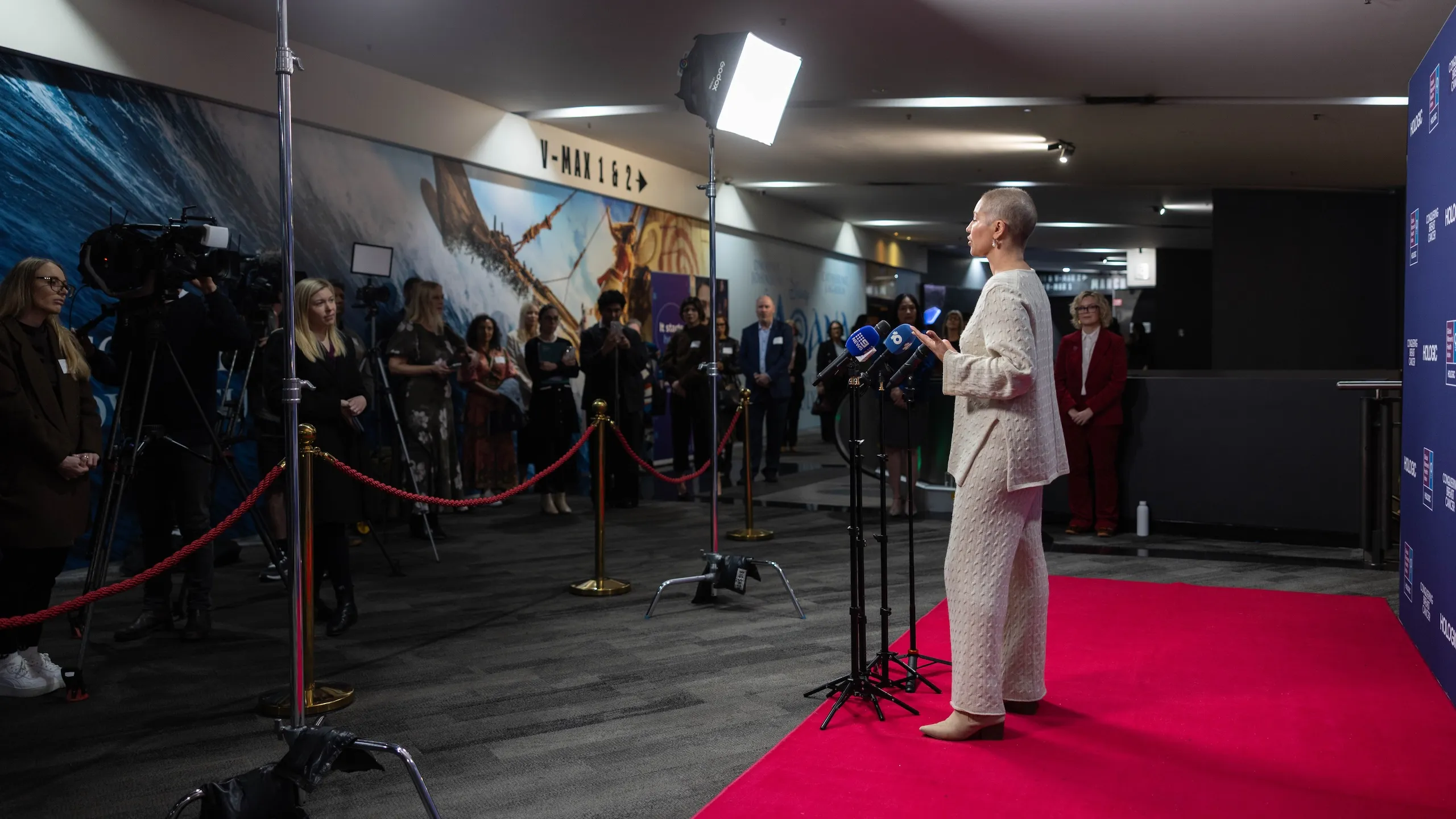 A lady facing cameras and microphones in front of a media wall